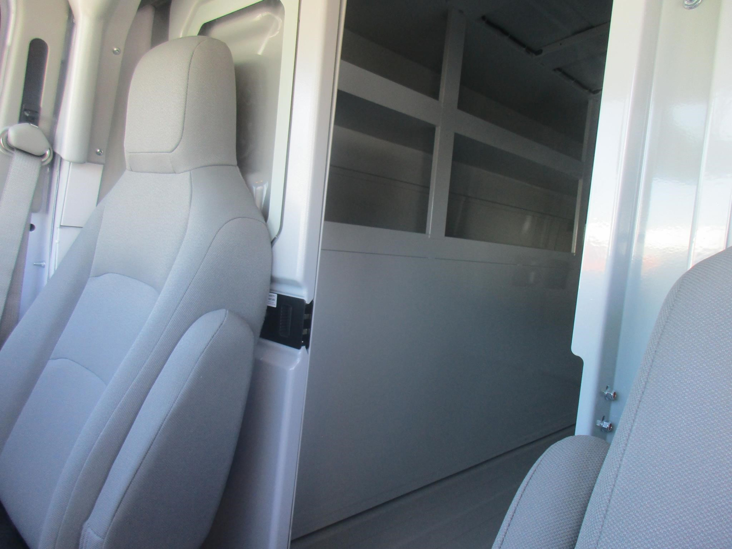 Ford E-350 cargo van interior showing partition wall and seating area with light gray upholstery.