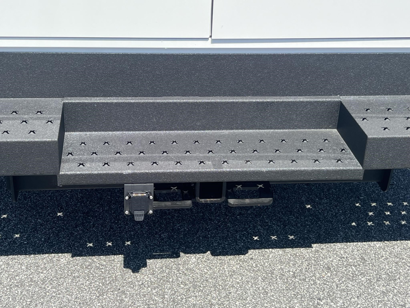 Ford E-350 service body rear step bumper with trailer hitch and receiver; textured black step surface visible.