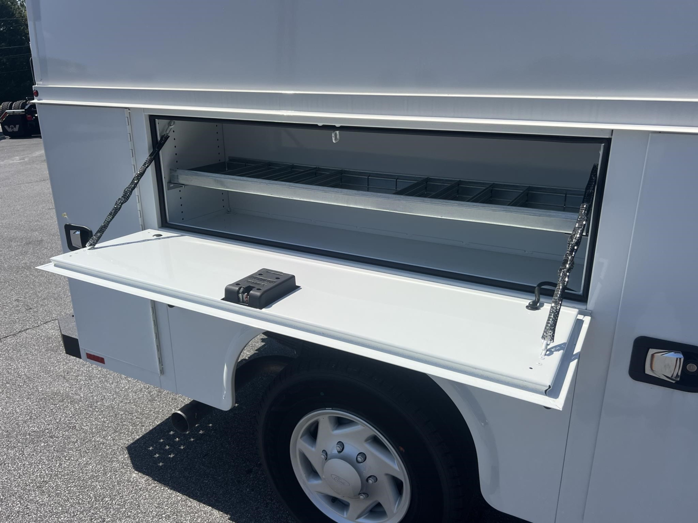 Ford E-350 service body side storage drawer open showing empty rack and pull-out tray.