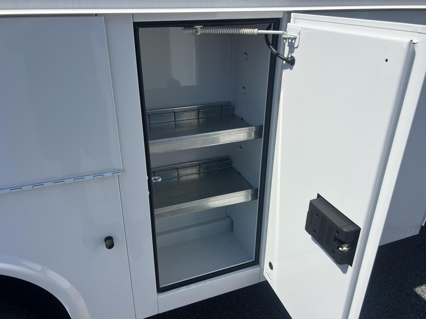 Open storage cabinet on utility truck showing shelves and interior with metal support brackets.