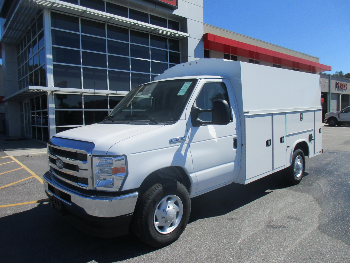 Ford E-350 service utility van with large white cargo body, front grille, and side compartments parked outside dealership.