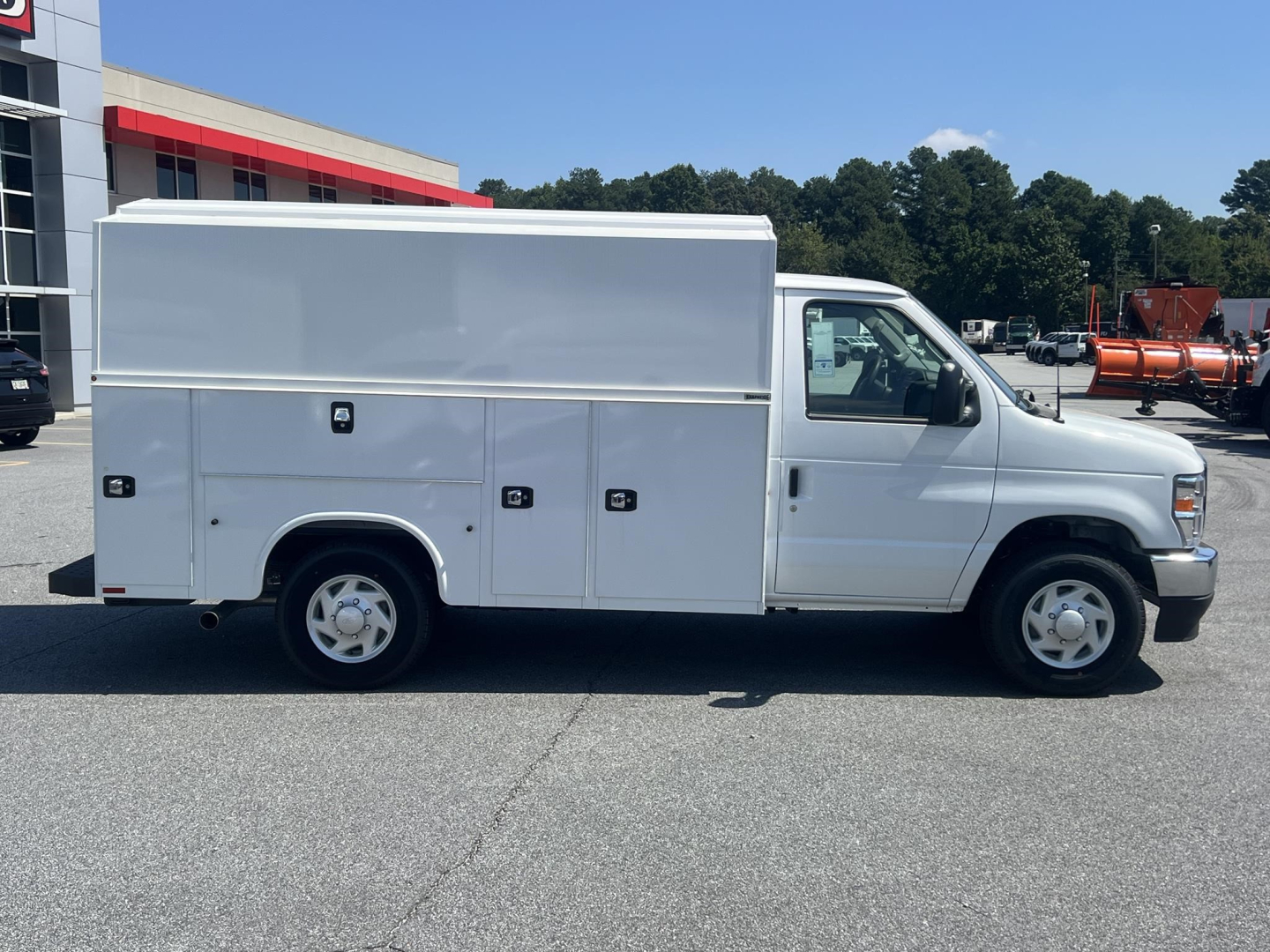 Side view of a white Ford E-350 service utility van with multiple external storage compartments along the side, cargo box on rear, standard dual rear wheels, and a single cab. No visible branding beyond generic Ford emblems.