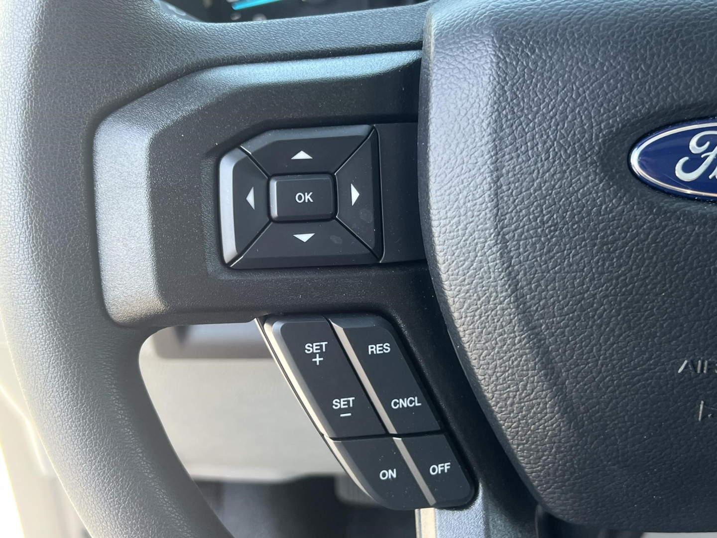 Ford steering wheel with cruise control buttons and directional pad on left side, part of a new 2026 Ford E350 interior view.