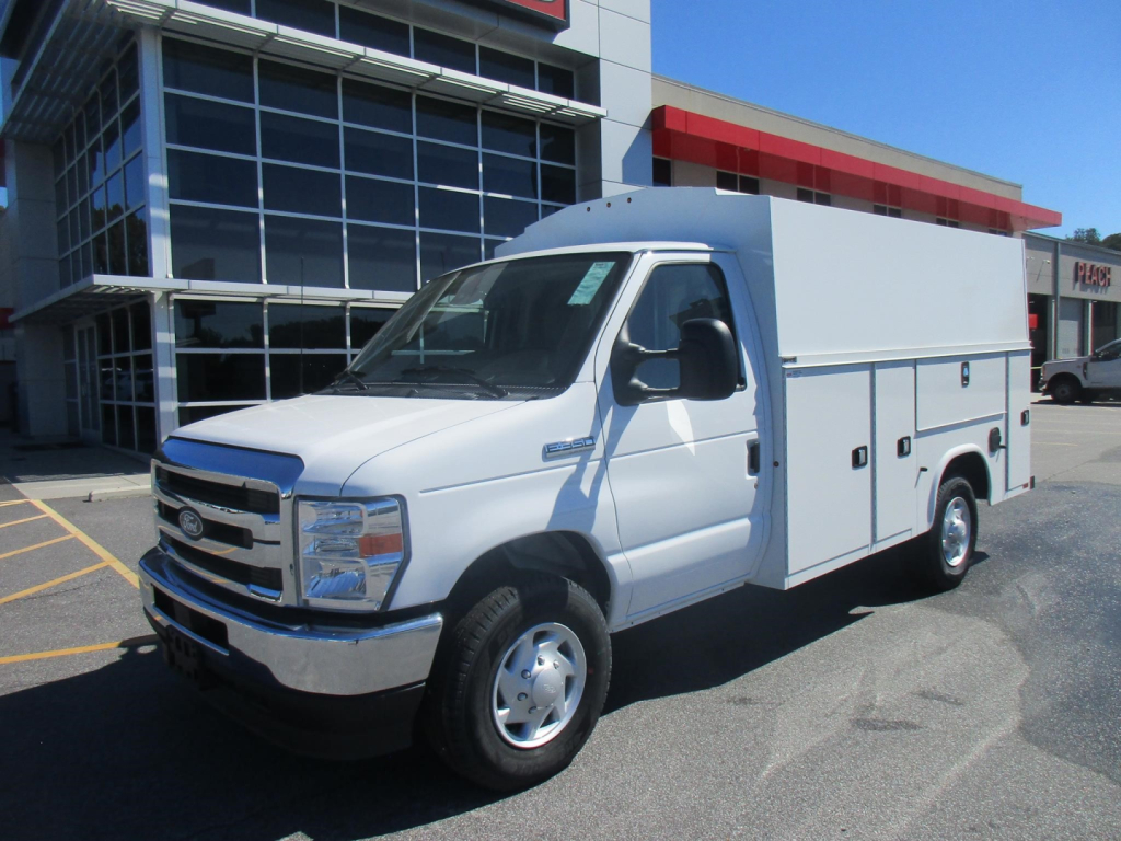 Ford E-350 service utility van with large white cargo body, front grille, and side compartments parked outside dealership.