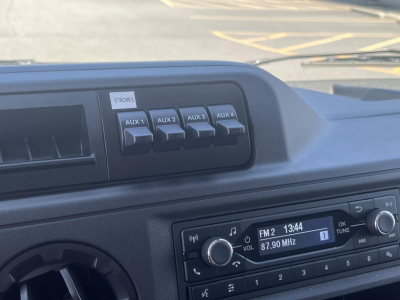 Ford E-350 dash showing auxiliary switches labeled AUX 1 to AUX 4 and radio display tuned to FM2 87.90 MHz.