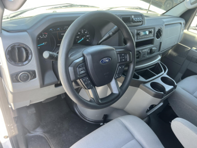 Ford E-Series van interior showing steering wheel with Ford badge, dashboard, and center console with cup holders.