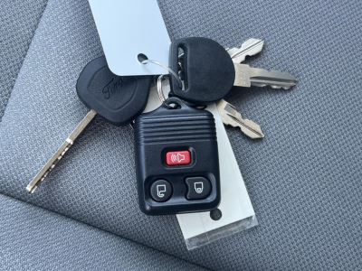 Key fob with three buttons resting on car seat showing lock/unlock buttons and ignition key along with two metal keys