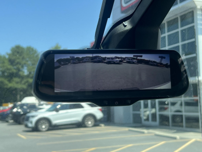 Rearview mirror-style display showing a vehicle rear camera feed in a Ford E-350 service/utility truck window reflection.