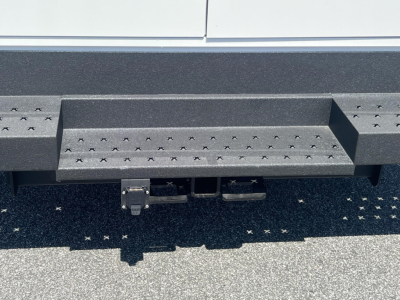 Ford E-350 service body rear step bumper with trailer hitch and receiver; textured black step surface visible.
