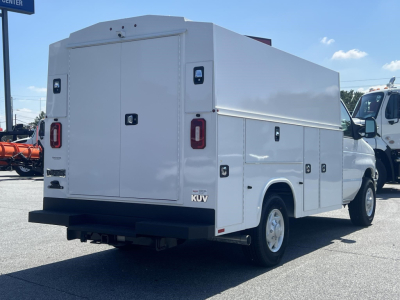 Utility service van rear and side compartments with storage doors and KUV branding; white box truck on dealership lot.