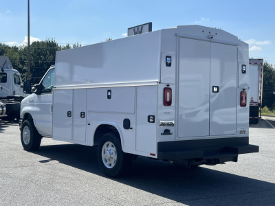 Ford E-Series utility van with storage compartments and rear doors, side cabinet doors visible, white utility body.