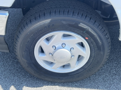 Ford E-350 wheel and tire close-up showing tire tread and hubcap; partial front fender visible.
