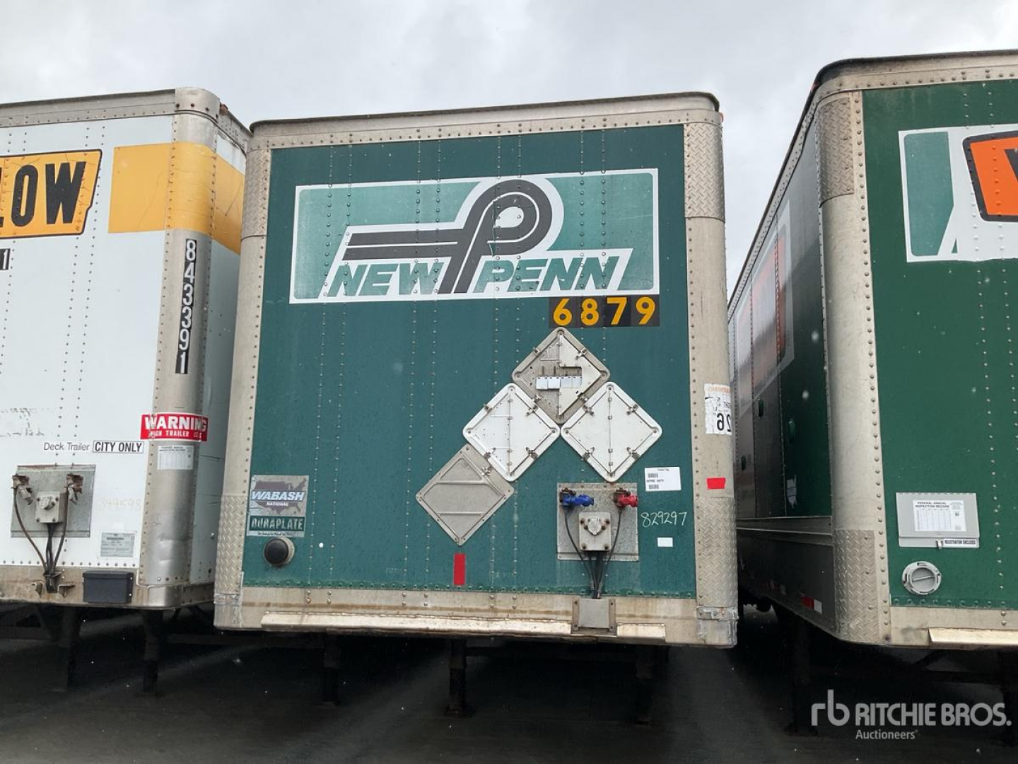 New Penn logo on green trailer back door with diamond-shaped reflective markings and rear latch; other trailers visible on sides.