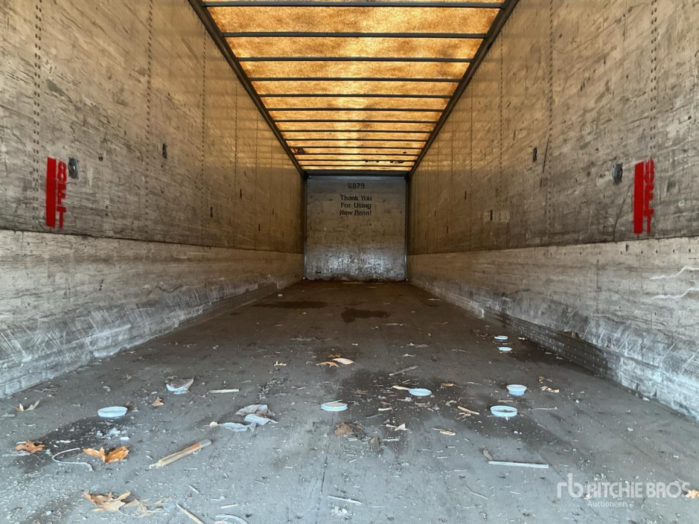 Trailer interior showing empty cargo area with dirt and debris, wood sidewalls, and overhead lighting.