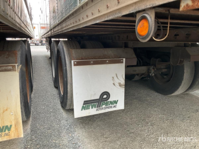 Trailer side view showing New Penn mudflap and dual wheels under trailer with orange side marker, metal frame, gravel ground.