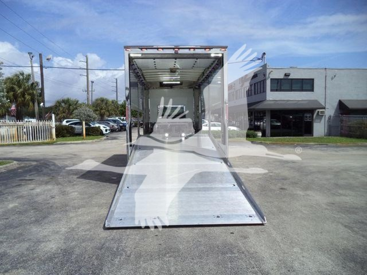 Trailer interior with open ramp extending to ground, rear doorway with bright interior lighting.