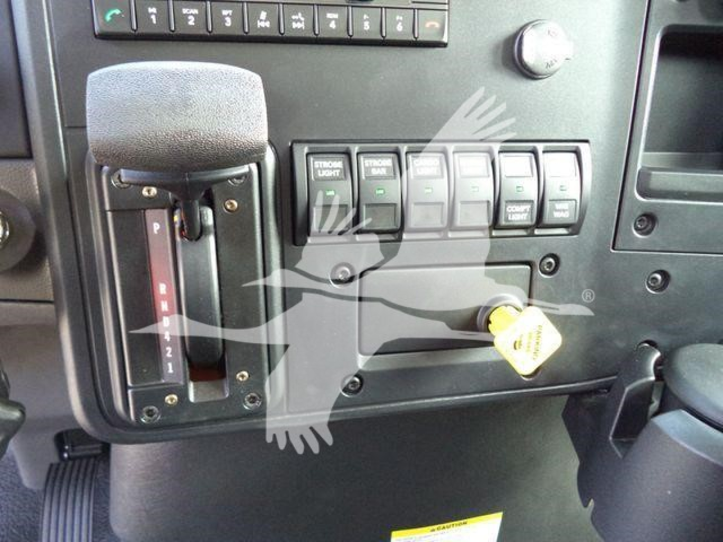 Cab interior of a 2027 International MV rollback truck showing gear shifter, control switches, and ignition key slot.
