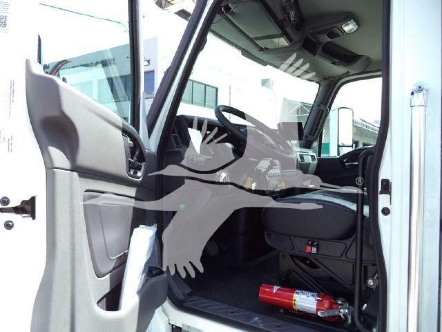Cab interior of a new 2027 International MV rollback truck showing steering wheel, dashboard, driver seat, and a fire extinguisher on the floor.