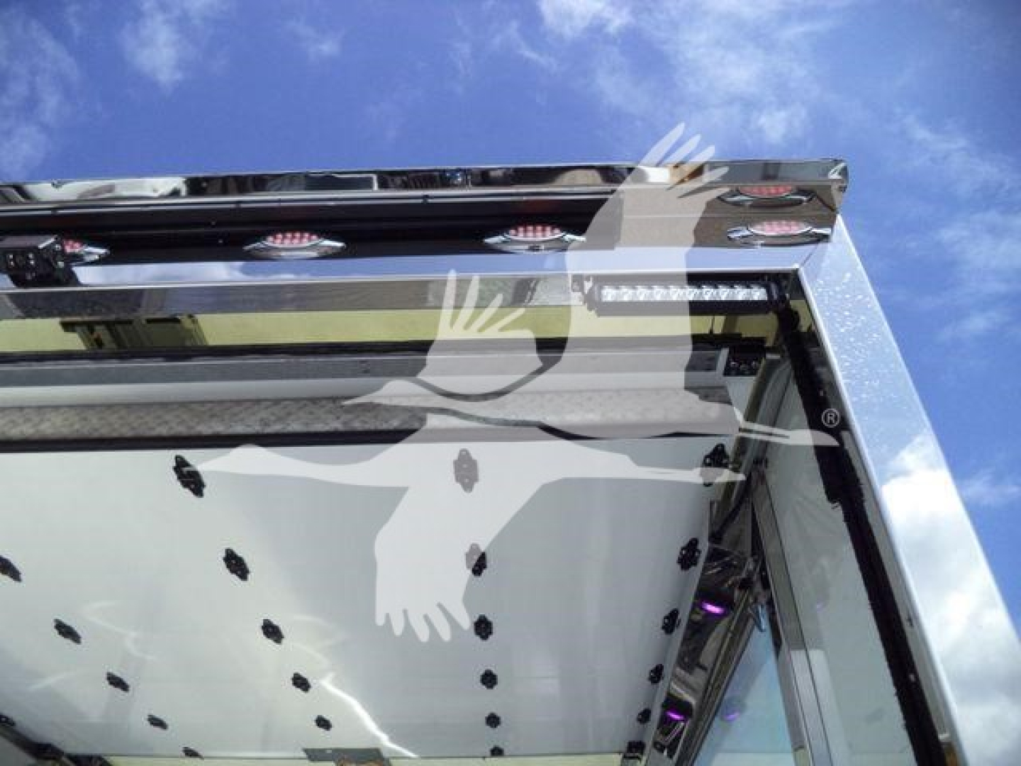 Truck rollback body showing chrome trim and reflection on side with grill area and white delivery truck roof