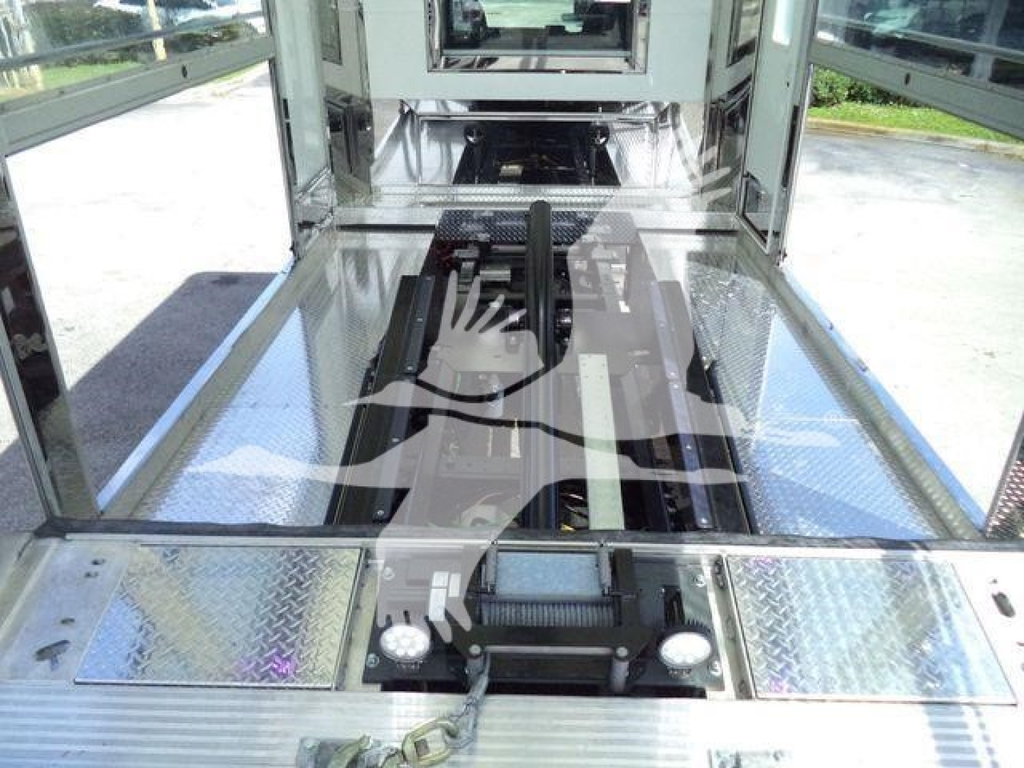 Truck bed area showing hydraulic winch and rear platform on a new International MV rollback truck; visible metal diamond plate surfaces and a central drive mechanism.