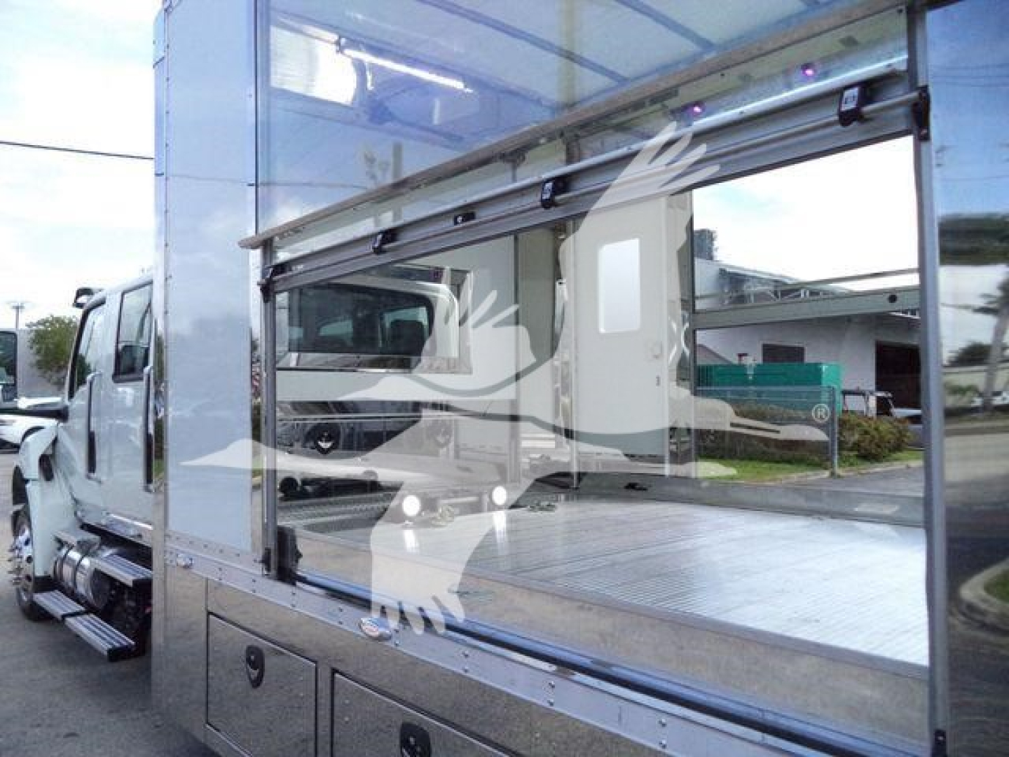 Truck bed area of a 2027 International MV rollback truck showing aluminum flatbed with side windowed cargo area and reflective metal surfaces.