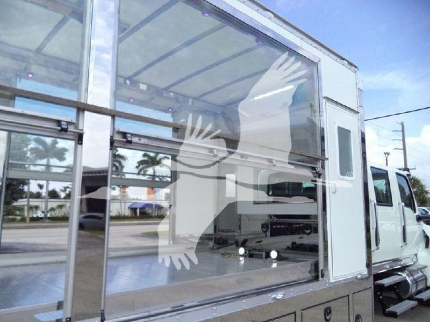 Vehicle cargo area in a rollback truck showing a large glass side panel and aluminum storage, with white cab in background.