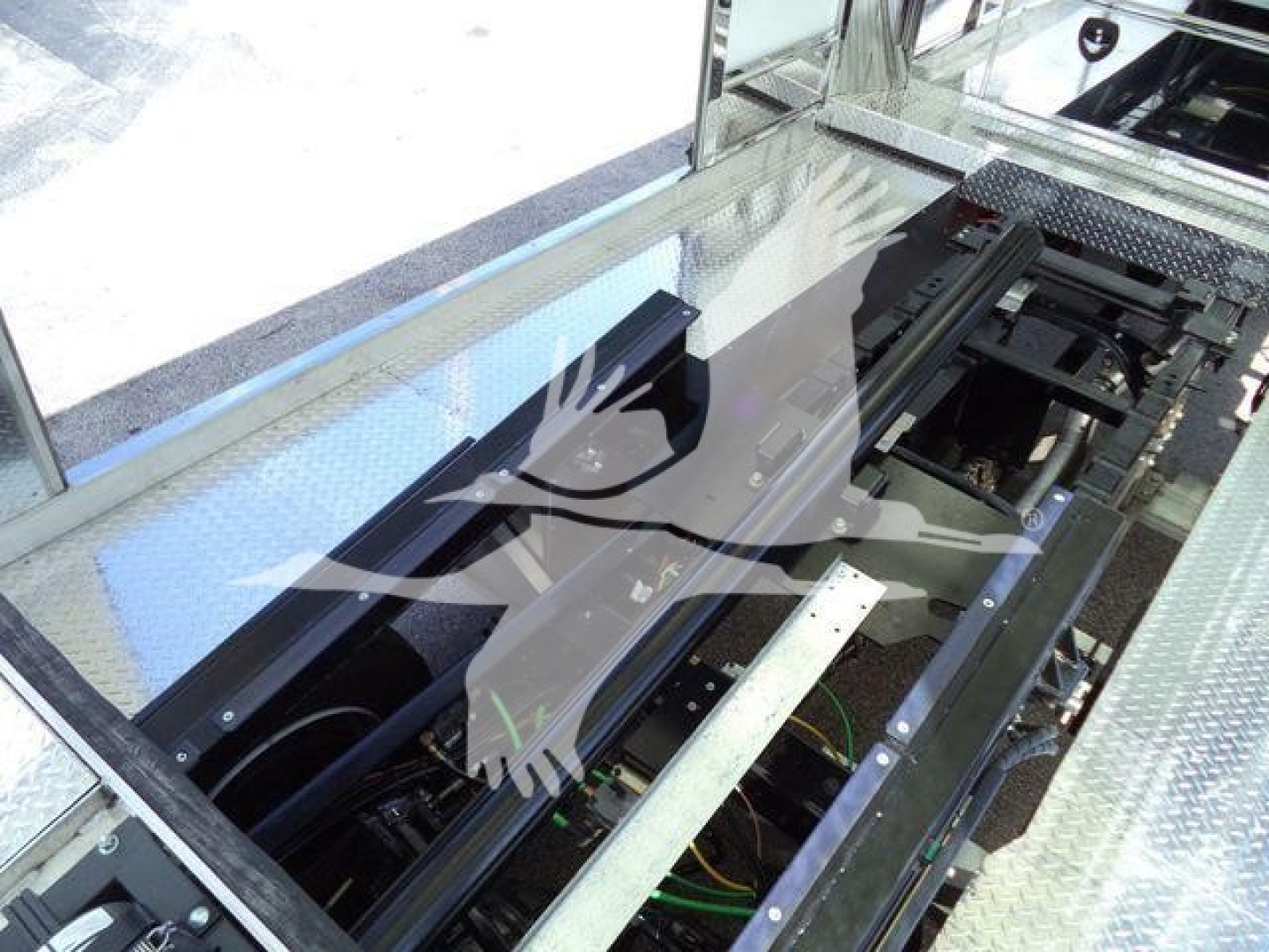 Truck rollback platform showing hydraulic assembly and chassis components with metal diamond-plate flooring and rails.