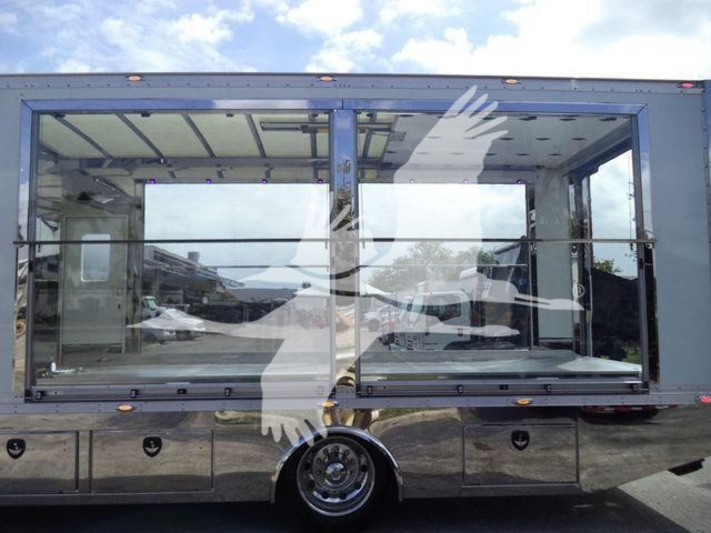 Truck rollback body side with large glass windows showing interior seating and chrome/metal storage compartments beneath; reflection of surroundings in the glass.