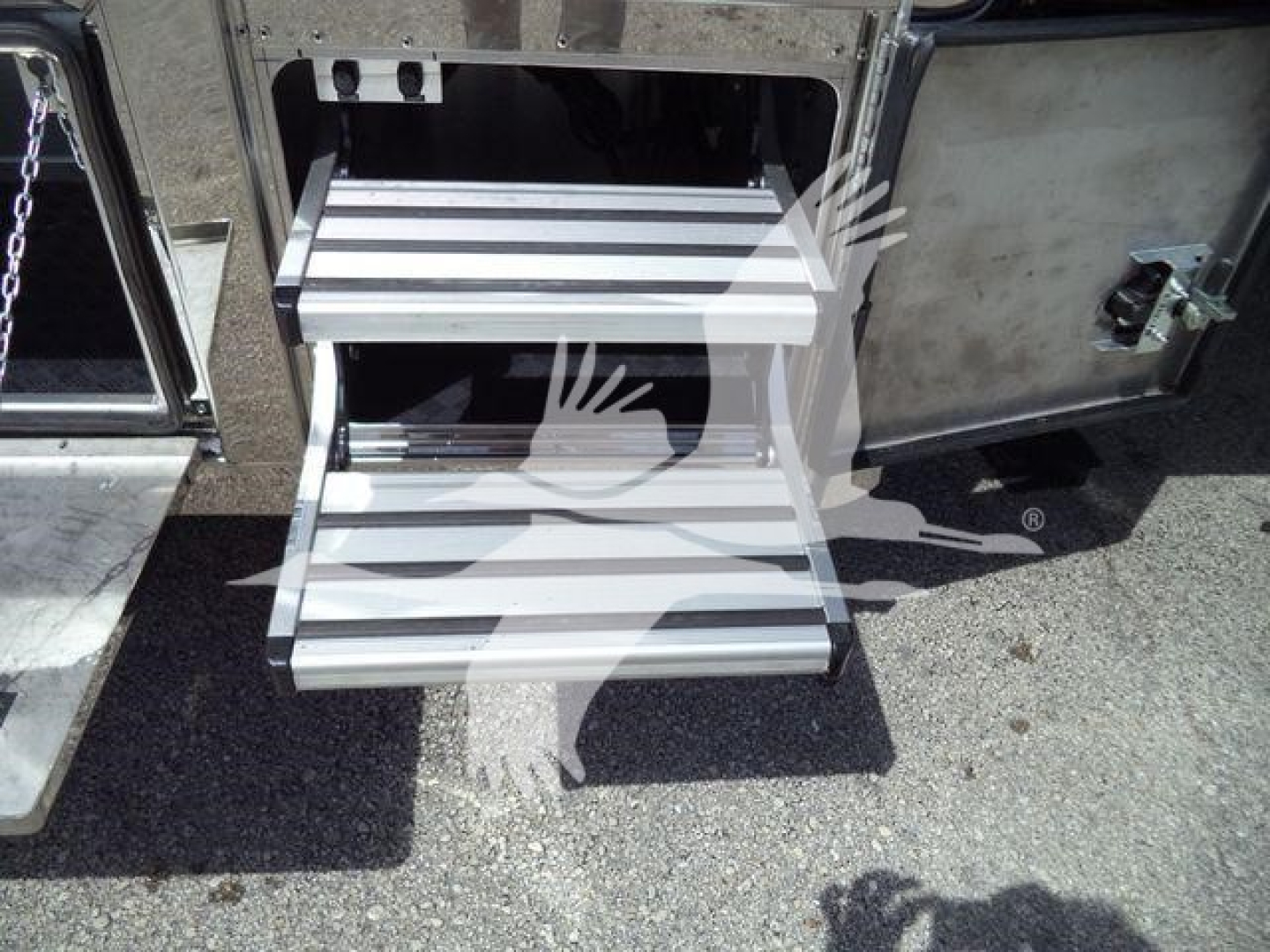 Two metal stairs and side of a truck with a chain and latch visible. Steps show ribbed aluminum treads and drop-down access panel.