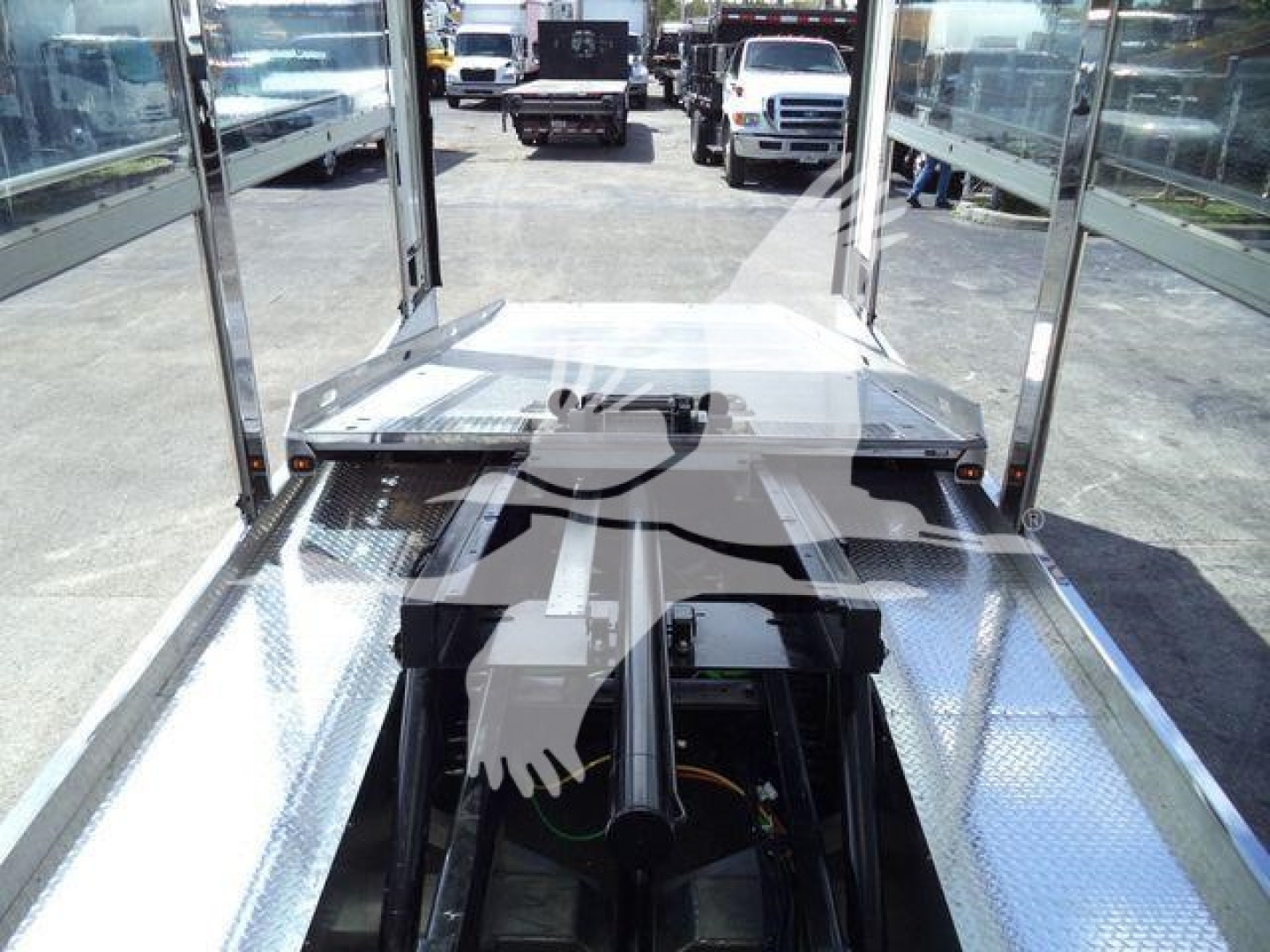Truck trailer platform showing aluminum flooring and rear hitch with metal step, long wheelbase, and cab visible in background.
