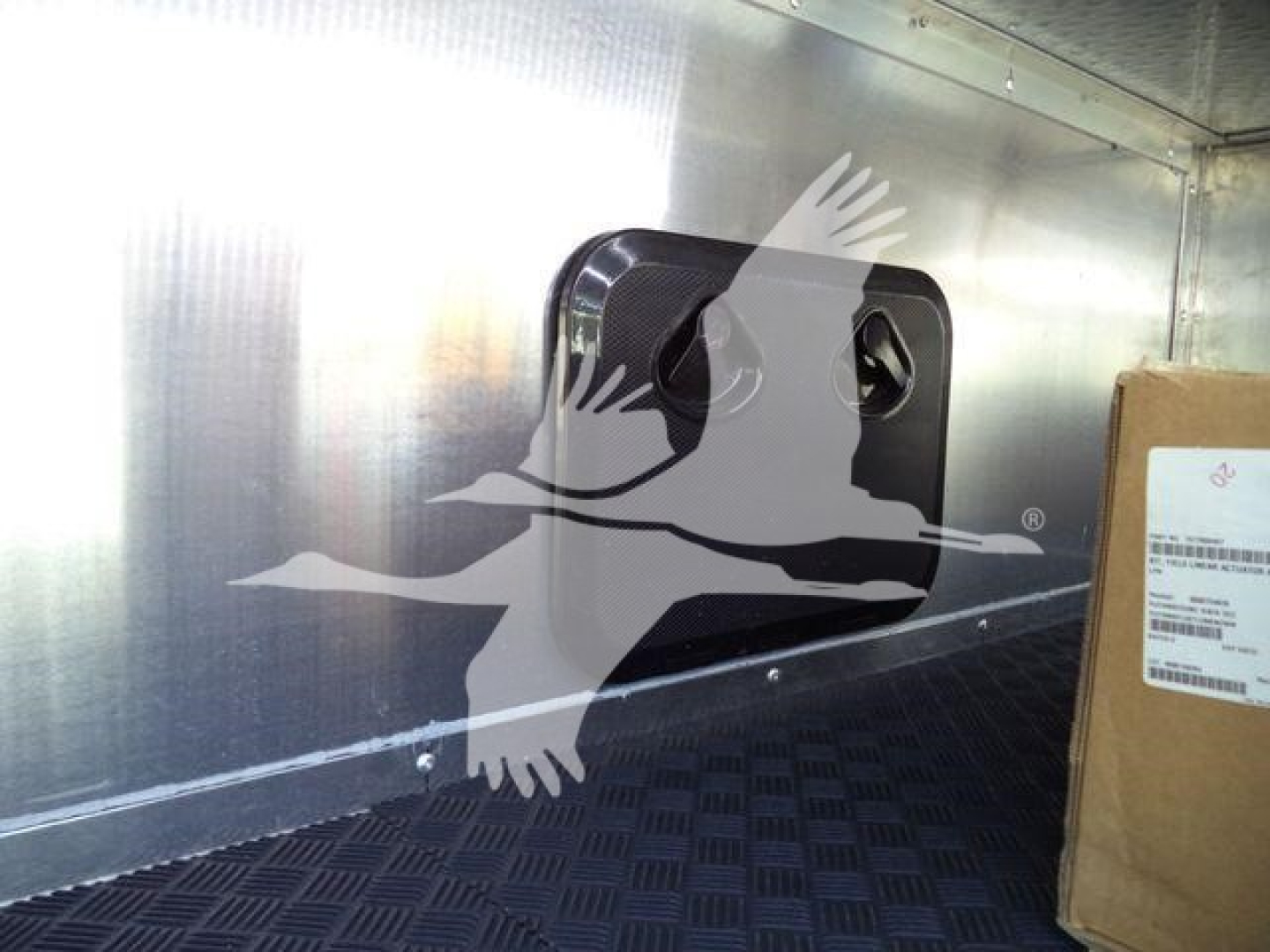 Truck interior showing a black square vent or access panel on a metal sidewall with a cardboard box nearby.