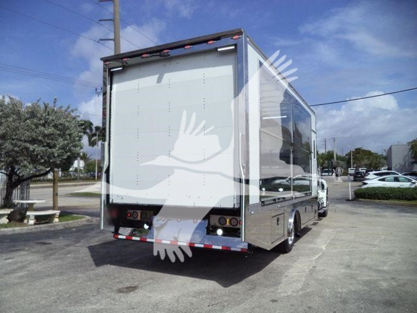Box truck rear and side with clear panels, white body, black bumper, and taillights visible; truck is parked in lot.