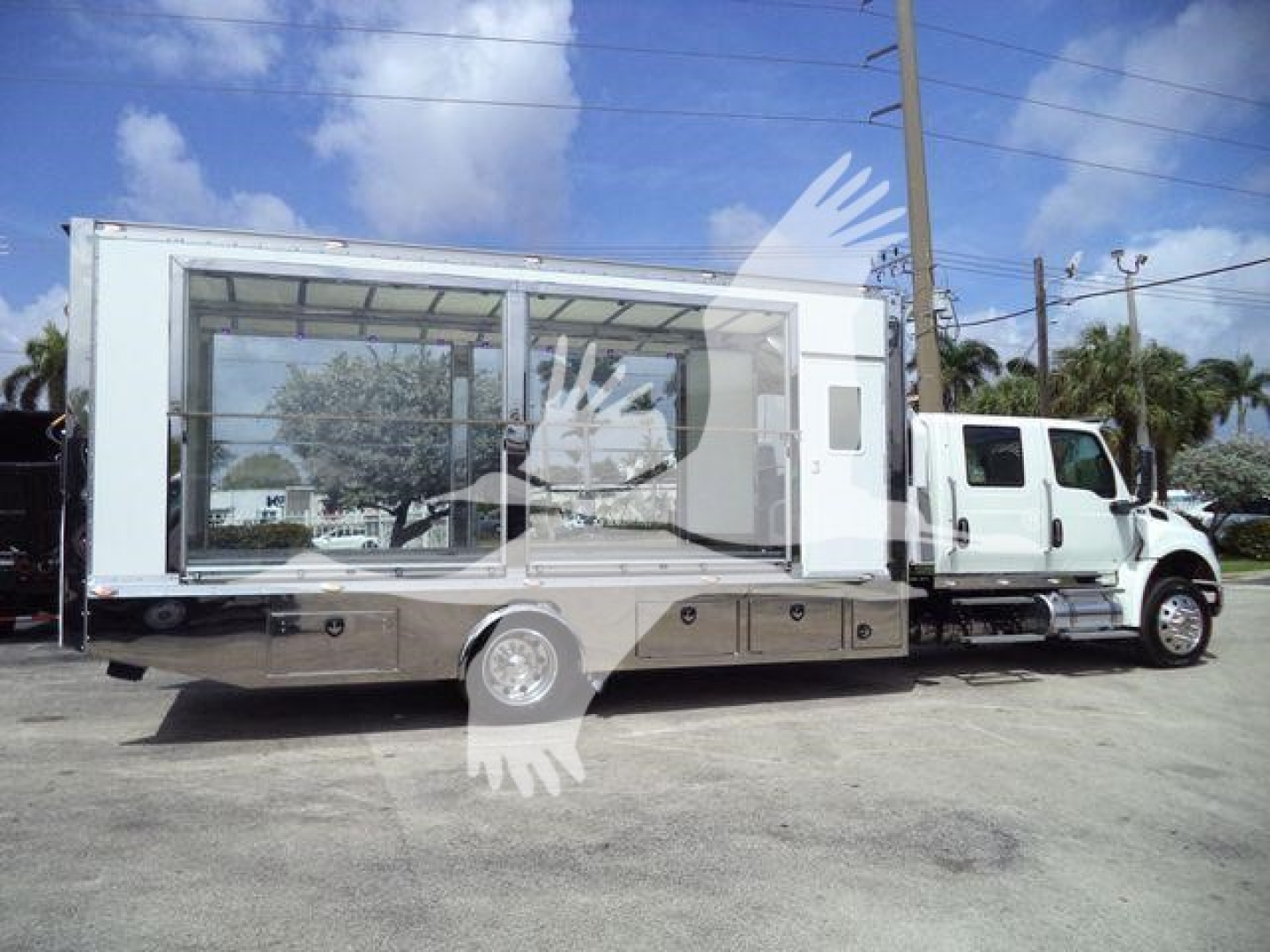 Truck-mounted rollback with large glass-walled passenger/cargo area on the back of a medium-duty International MV truck, side view.