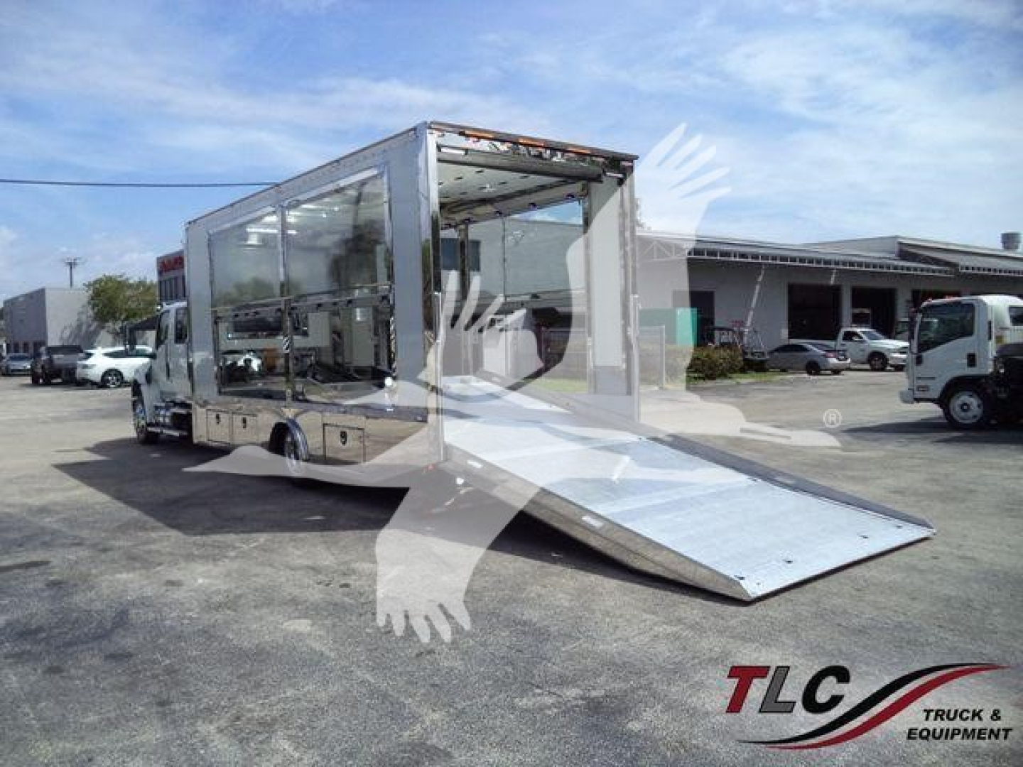 Truck bed with wheelchair-accessible ramp and glass-sided cargo area, International MV rollback truck in a lot.