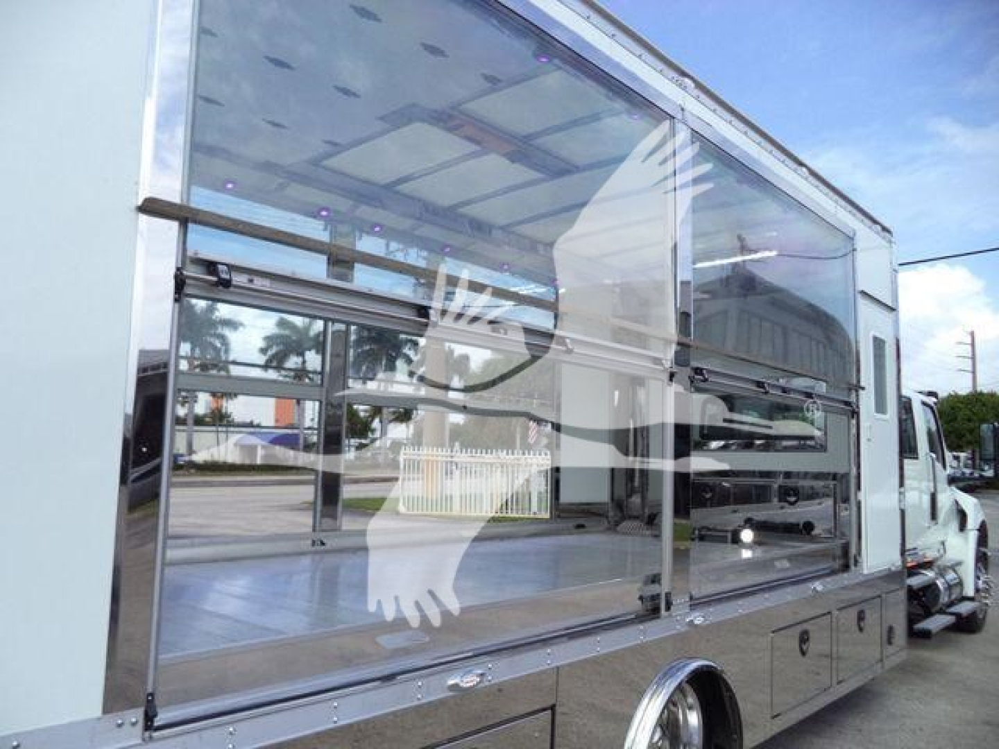 Truck body side view showing large glass display and service compartment on a rollback truck, chrome frame, reflection of surroundings in glass.