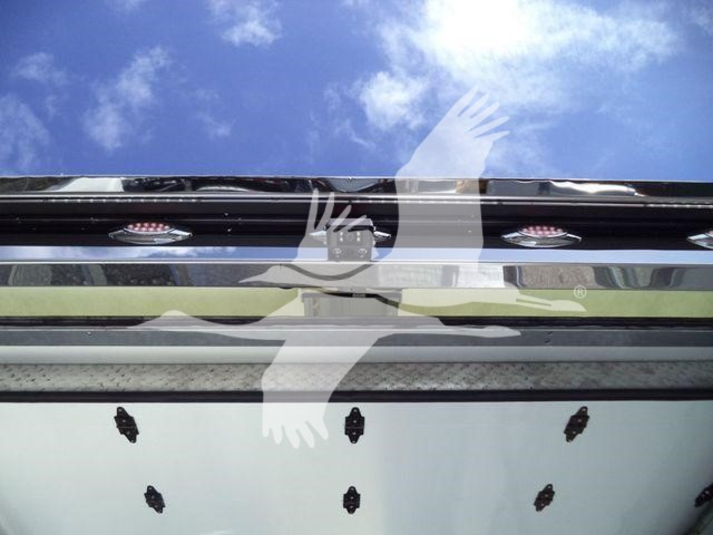 Truck tailgate area with reflection of the sky; small black label stickers on bumper.