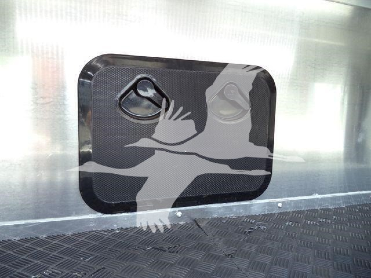 Trailer side window with two circular vents and a protective panel; metal surface and diamond plate floor visible.