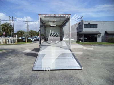 Trailer interior with open ramp extending to ground, rear doorway with bright interior lighting.