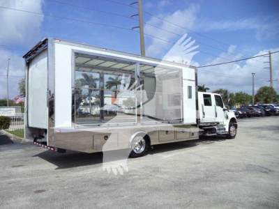 Truck-mounted mobile showroom/box truck with large glass display windows on side, International MV chassis, white and chrome accents, parked in a lot.