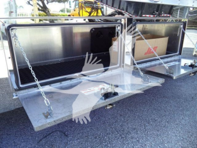 Truck rollback bed storage compartments open showing metal compartments with chains and a cardboard box inside; dual hinged lids and shiny metal surface.