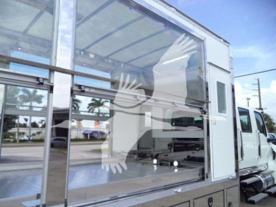 Vehicle cargo area in a rollback truck showing a large glass side panel and aluminum storage, with white cab in background.