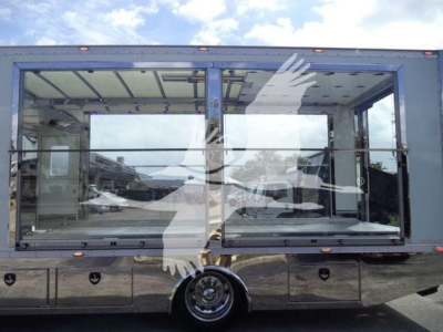 Truck rollback body side with large glass windows showing interior seating and chrome/metal storage compartments beneath; reflection of surroundings in the glass.