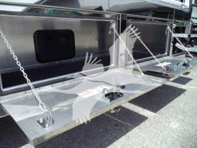Truck rollover bed with metal steps and chains, storage compartments, and instructional labels visible on a flatbed trailer