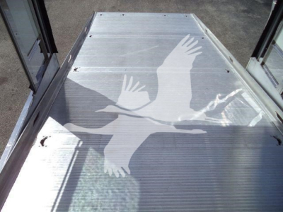 Metal truck bed with silver corrugated surface and a white graphic of two birds in flight. Side rails and glass doors frame the area.