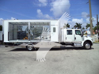 Truck with a large rectangular cargo area mounted on a white International MV chassis, side view, showing glassed interior compartment and open sliding door.