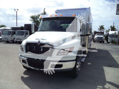 White International MV truck in a dealership lot, front view, with cargo box on chassis and other trucks in background.
