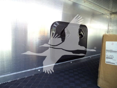 Truck interior showing a black square vent or access panel on a metal sidewall with a cardboard box nearby.