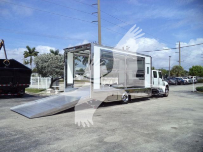 Truck-mounted mobile showroom with loading ramp, International MV body, side windows, front cab visible, outdoor dealership lot.