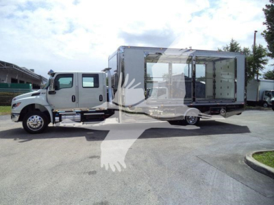 Flatbed truck with a large rectangular living/box cab on a matching truck chassis, the box features large glass windows and doors on the side; a white semi-truck with a chrome front and black tires.