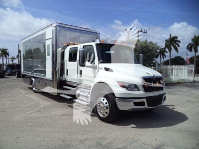 Truck cab with attached large rectangular cargo area, white International MV model, rollback truck, side view showing cab and cargo container.